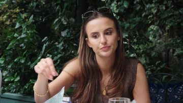 a woman sitting at a table engaged in conversation amidst lush greenery