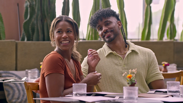 couple seated at a restaurant table with plants in the background