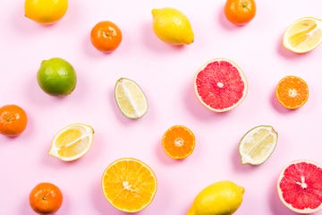 Several kinds of whole and cut citrus on a pink background