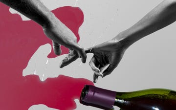 a couple hands with their pinky fingers interlocked over a spilled bottle of wine