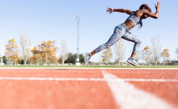 sportswoman with dedication running on sports track against clear sky during sunny day