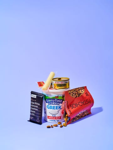 multiple snacks, such as string cheese and pistachios, on a blueish purple background