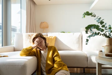 woman having headache and holding her head while sitting on the floor at home