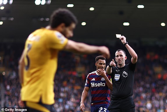 WOLVERHAMPTON, ENGLAND - SEPTEMBER 15: Referee Chris Kavanagh shows Rayan Ait-Nouri of Wolverhampton Wanderers (obscured) a yellow card during the Premier League match between Wolverhampton Wanderers FC and Newcastle United FC at Molineux on September 15, 2024 in Wolverhampton, England. (Photo by Naomi Baker/Getty Images)