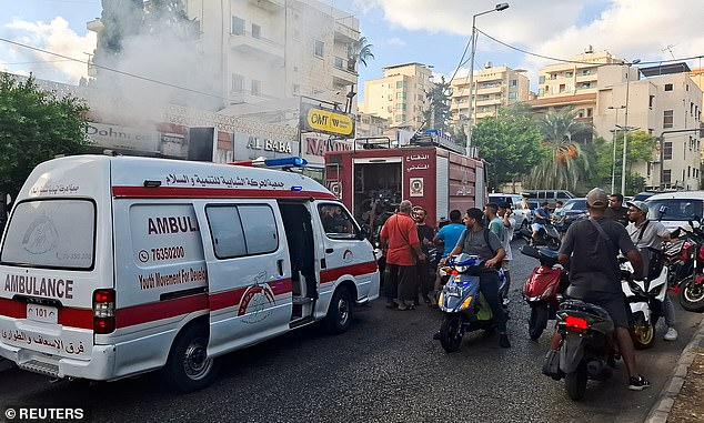 People gather as smoke rises from a mobile shop in Sidon, Lebanon on September 18