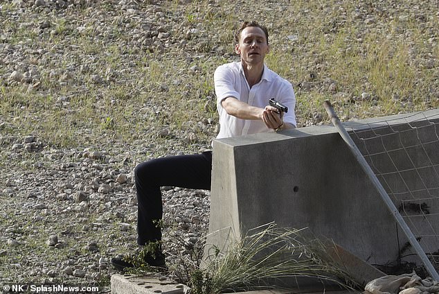 Tom Hiddleston appears with a gun in hand as he is seen on the set of The Night Manager