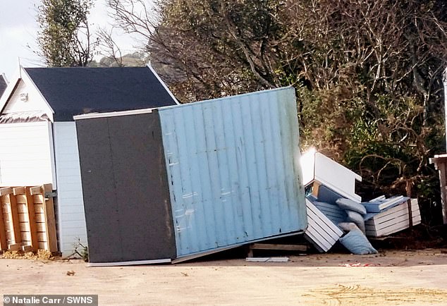 A beach hut is seen damaged with furniture falling out of it after the landslide