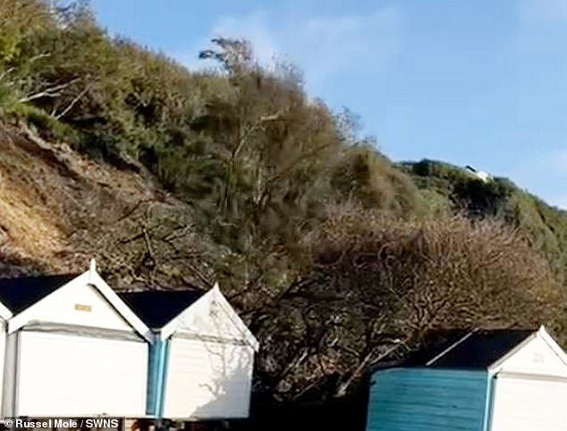 Piles of earth are seen falling down onto beach huts in Bournemouth during a landslide