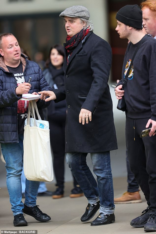 The Libertines star, 45, cut a smart figure in a black trench coat layered over a baggy pair of blue jeans