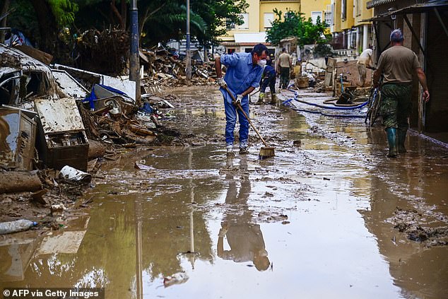 A man uses a broom to clear mud from a street following devastating floods in Alfafar