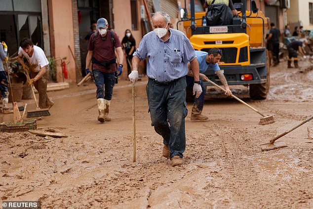 People remove mud from a road following heavy rains in Paiporta, near Valencia