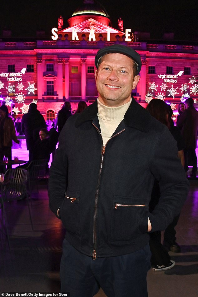 Dermot bundled up in a black jacket and cream turtleneck top, teamed with chinos, brown Chelsea boots and a flat cap