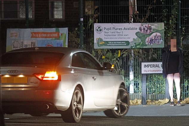 A suspected sex worker standing by the gates of Mount Pleasant Junior School on Thursday night as a car drove past