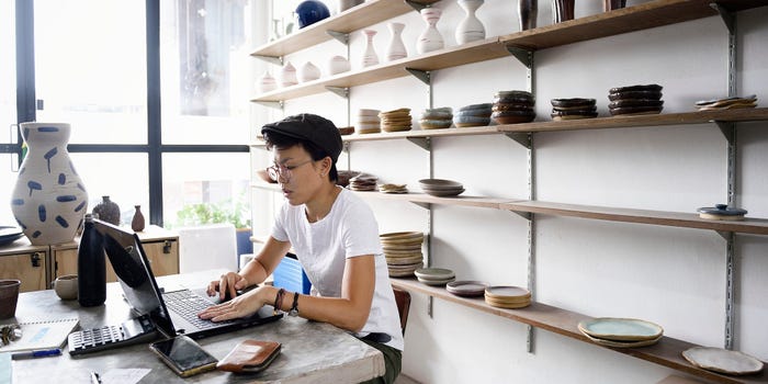 A worker sitting at a desk in a shop checks the average American debt on their laptop.