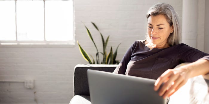 Middle-age woman sitting on couch looks up IRA CDs on computer.