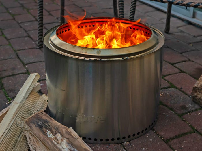 A stack of wood next to a Solo Stove Bonfire with a blazing fire in it.