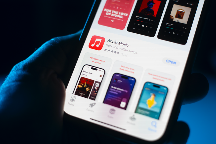 The Apple Music app is visible in the App Store on the screen of a phone in someone's hand