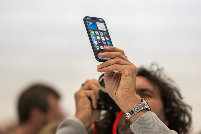 A man holds an iPhone in one hand and points a camera at it with the other hand