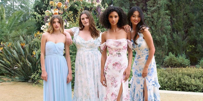 A bridal party of four in a garden wearing floral gowns.