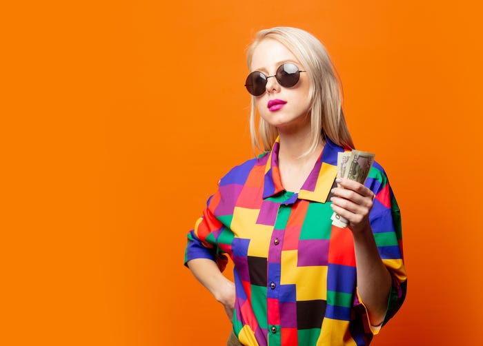 A young blond woman in a colorful shirt holding cash in front of an orange background.