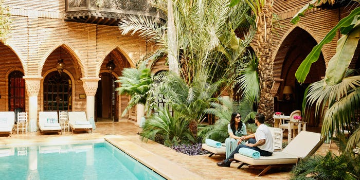 A couple chats by a small private aqua pool in a Moroccan riad surrounded by lush tropical greenery