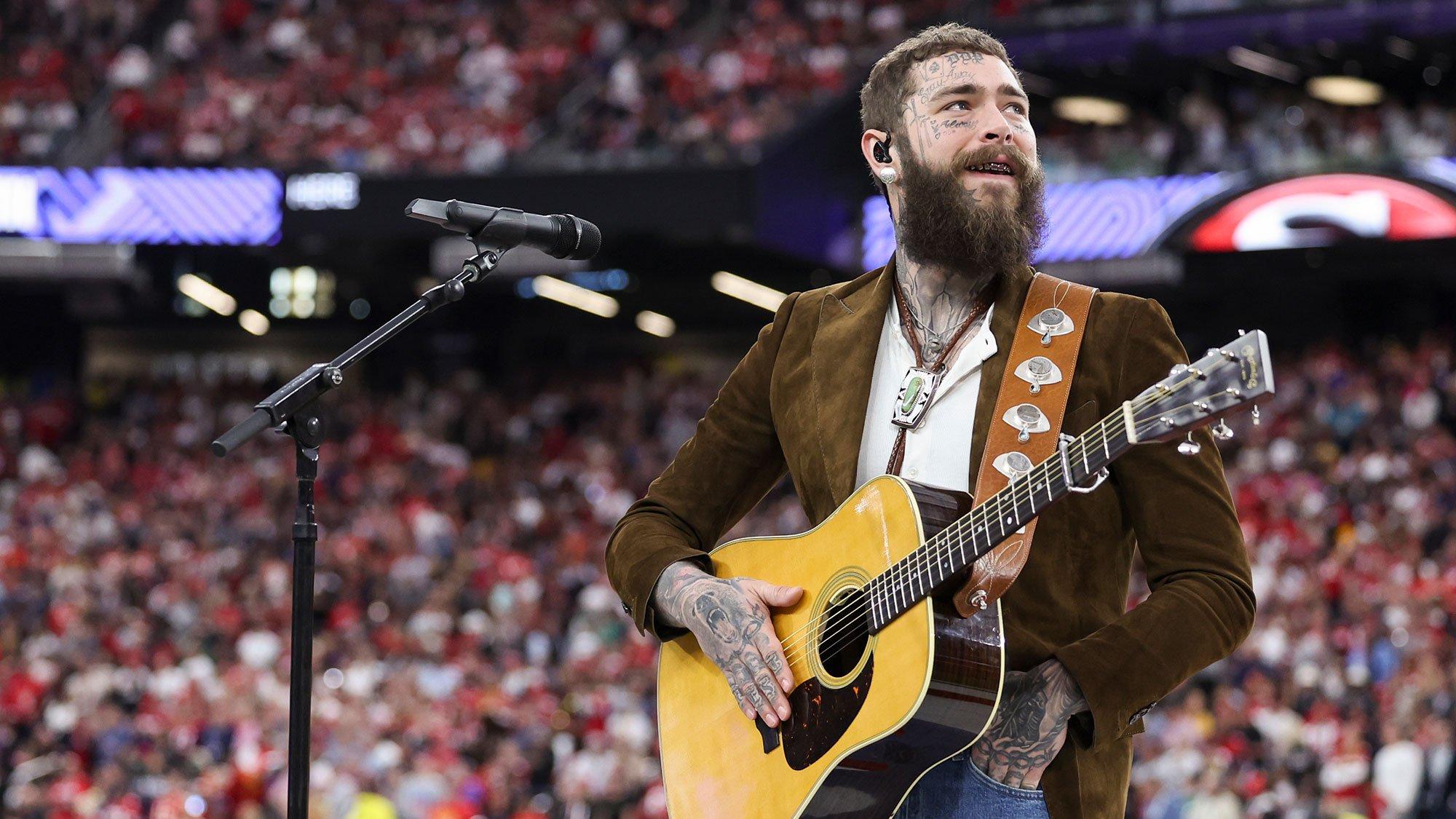 Post Malone holds and acoustic guitar and looks at the crown during his Super Bowl LVIII performance