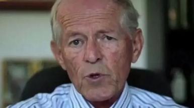 An image of John Smyth, wearing a striped white and purple collared shirt, facing the camera as he speaks.