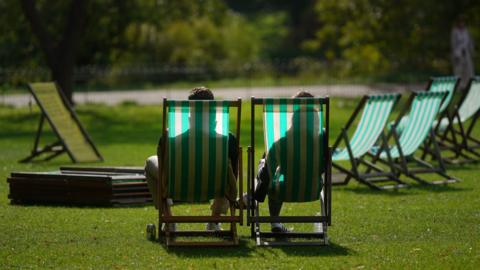 Two people in deckchairs seen from behind, in a sunny park