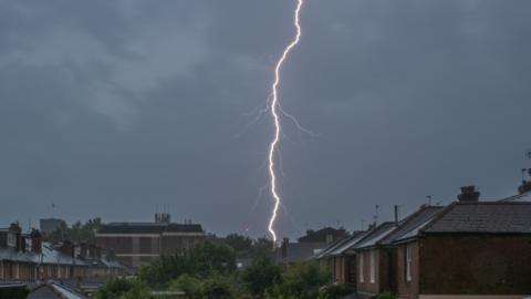 A single strike of lightning against a dark sky over rooftops