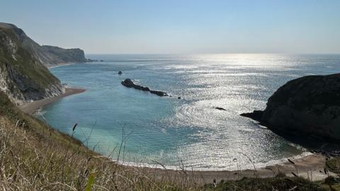 Coastal path view of beach with sun reflecting on sea