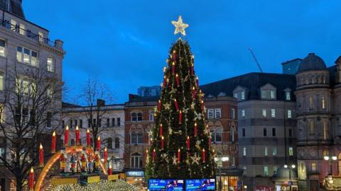 A huge Christmas tree with a market nearby in Birmingham city centre at dusk with blue sky behind