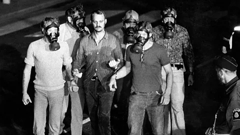 Men in gas masks handcuffed to central man, with police officer looking from the side (Credit: Getty Images)