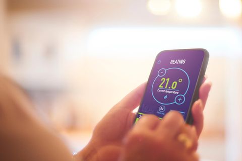 Smart-Thermostat: Eine Frau stellt an ihrem Smartphone per App die Heizung ein.