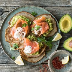 Ein Teller mit Pfannkuchen und Räucherlachs, daneben liegen Avocados