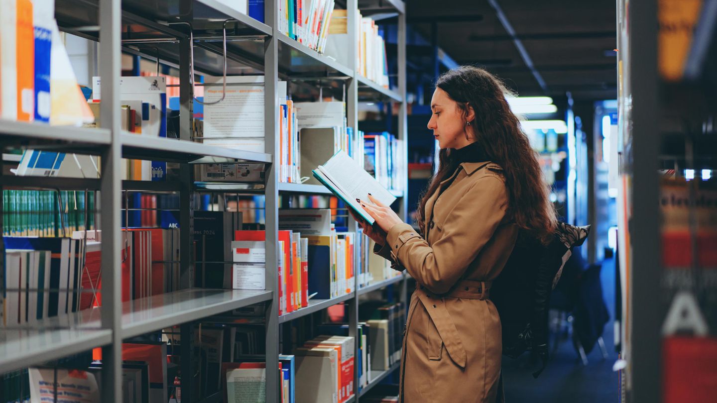 BAföG: Eine Studentin steht vor einem Regal in einer Bibliothek und liest in einem Buch