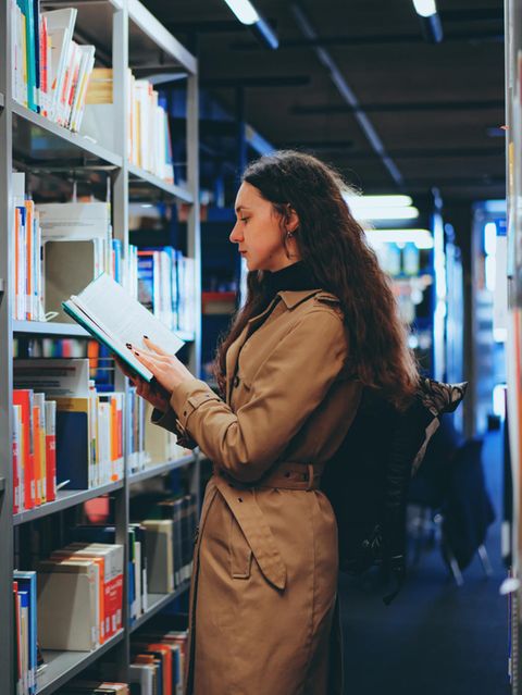 BAföG: Eine Studentin steht vor einem Regal in einer Bibliothek und liest in einem Buch