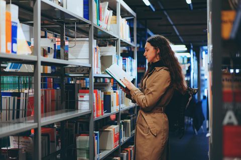 BAföG: Eine Studentin steht vor einem Regal in einer Bibliothek und liest in einem Buch