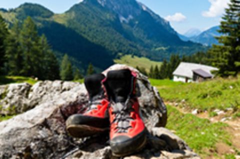 Wanderschuhe liegen auf einem Stein. Im Hintergrund sind Berglandschaften zu sehen.