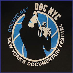 2012 DOC NYC Festival Shirt - blue and white image of a whoman with dark hair holding a handheld camera within a blue circle with text DOC NYC New York’s Documentary Festival DOCNYC.NET around the circle