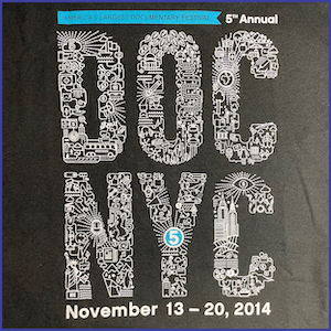 2014 DOC NYC Festival shirt - words DOC NYC shaped out of doodled images into letters, the words America’s Largest Documentary Festival on a blue banner and the words 5th Annual November 13-20, 2014 in white letters. Black shirt.