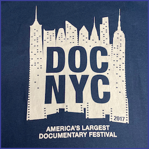 2017 DOC NYC Festival Shirt - White Ink image of city skyline with words DOC NYC and 2017 within the image. Words America’s Largest Documentary Festival in white ink under the skyline image. Dark Blue Shirt.