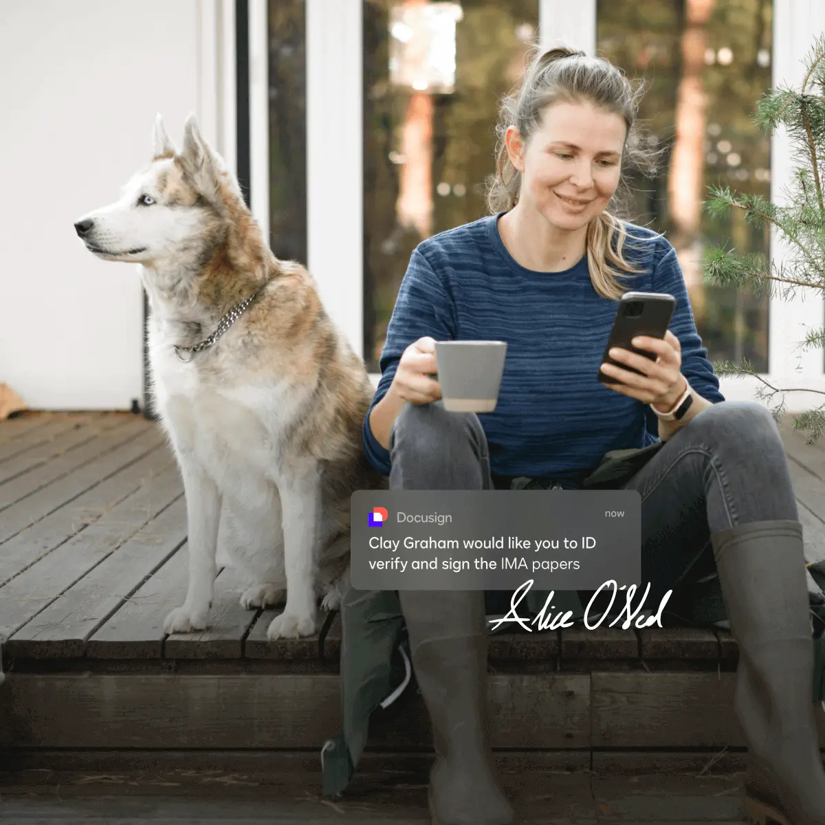 Woman with cup of coffee looking down at her phone next to a dog