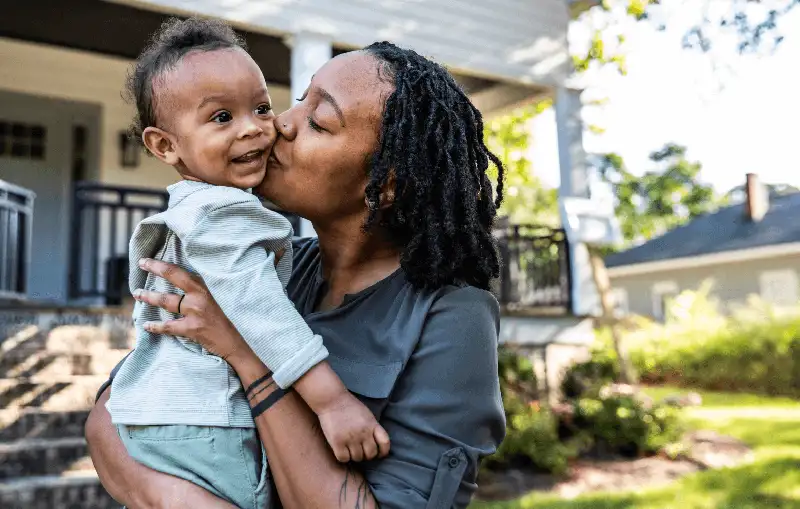 A woman kisses her child in front of their house