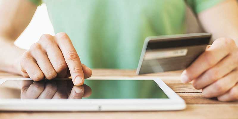 Close up on the hands of a person typing on a tablet while holding a credit card in the other hand