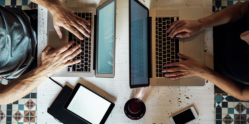 Overhead view of a table with two people working on laptops, next to two tablets and a smartphone