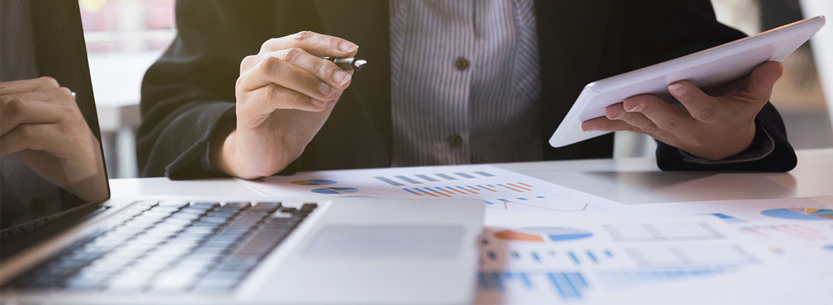 Businesswoman using a tablet while looking at printed reports