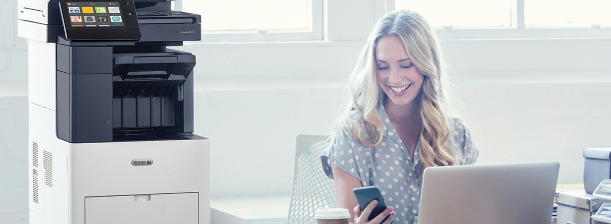 Happy woman with smartphone and laptop, sitting next to a Xerox MFP