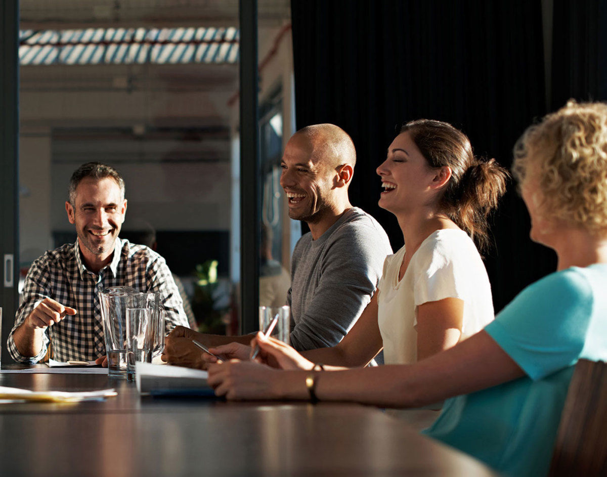 Colleagues laughing at a boardroom meeting table