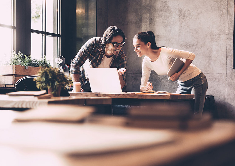 A man and woman leaning on a table, looking at a laptop