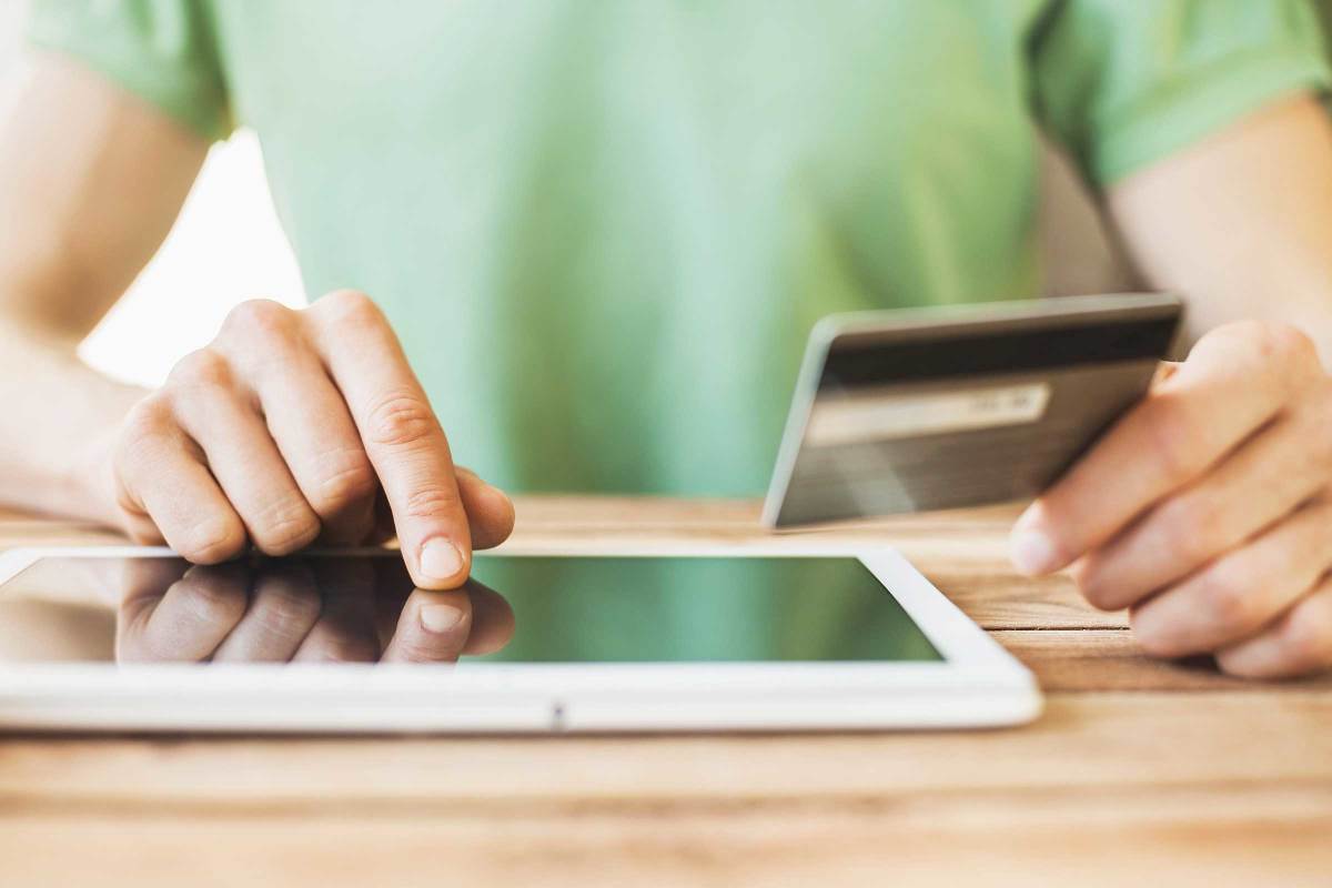 Close up on the hands of a person typing on a tablet while holding a credit card in the other hand